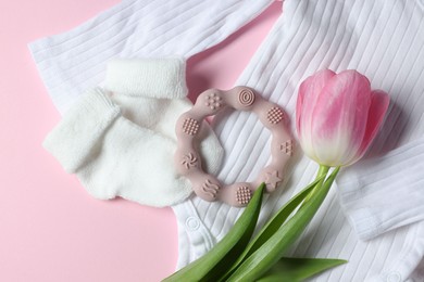 Baby onesie, socks, teether and tulip flower on pink background, flat lay