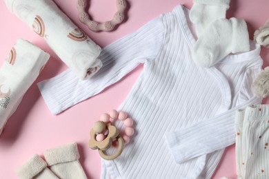 Baby clothes, toys and teether on pink background, flat lay