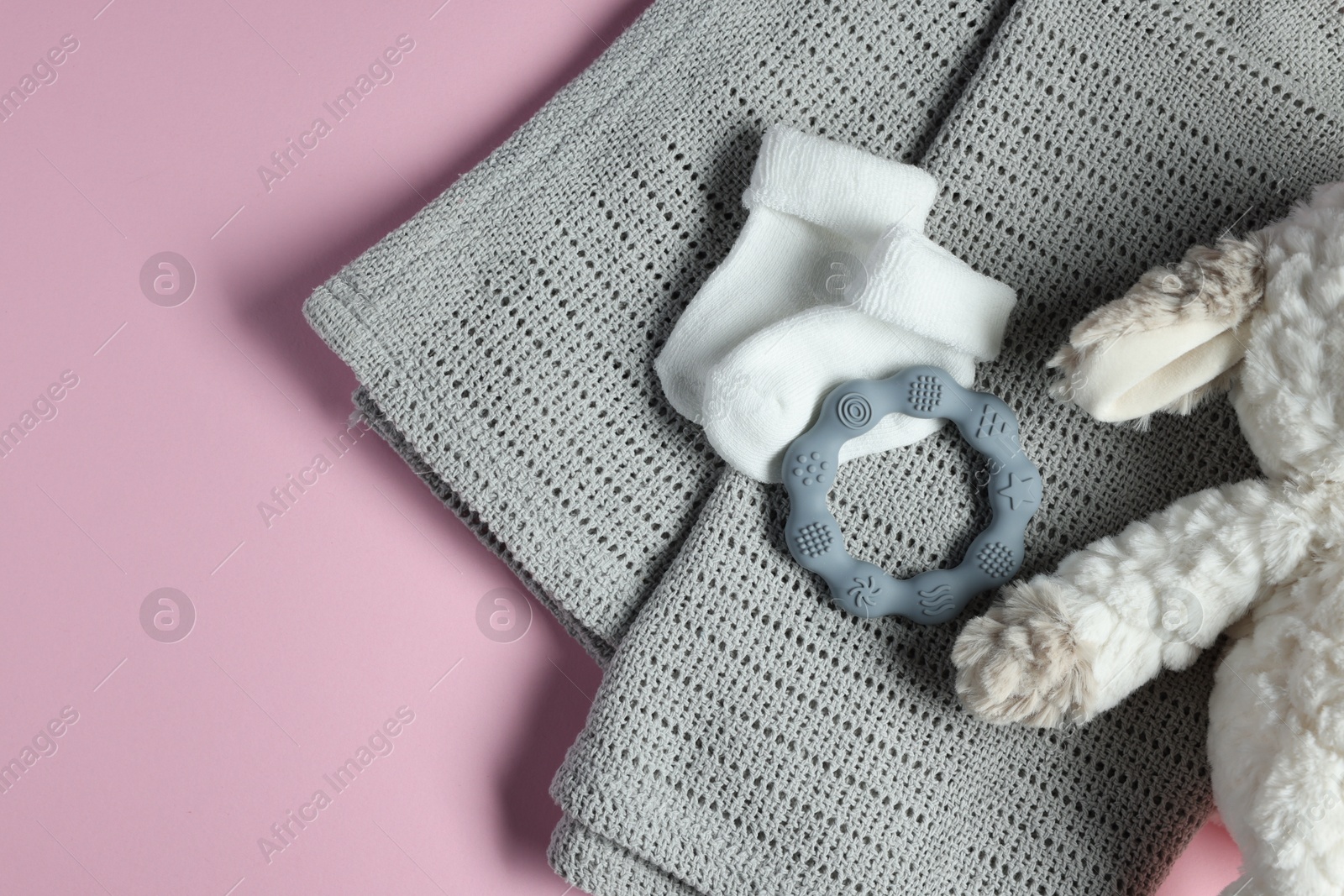 Photo of Towel, baby socks, teether and toy on pink background, flat lay