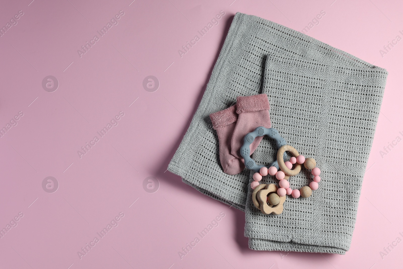 Photo of Towel, baby socks, teether and toys on pink background, flat lay. Space for text