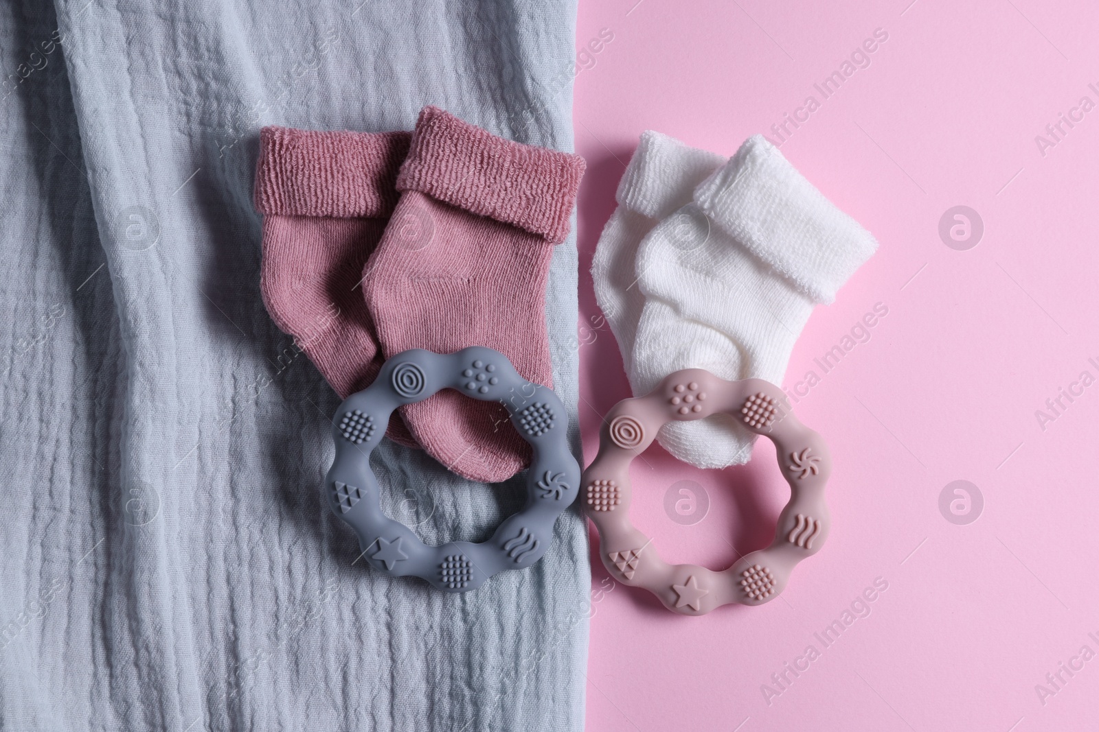 Photo of Baby blanket, socks and teethers on pink background, flat lay