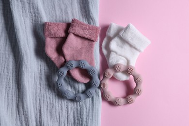 Photo of Baby blanket, socks and teethers on pink background, flat lay