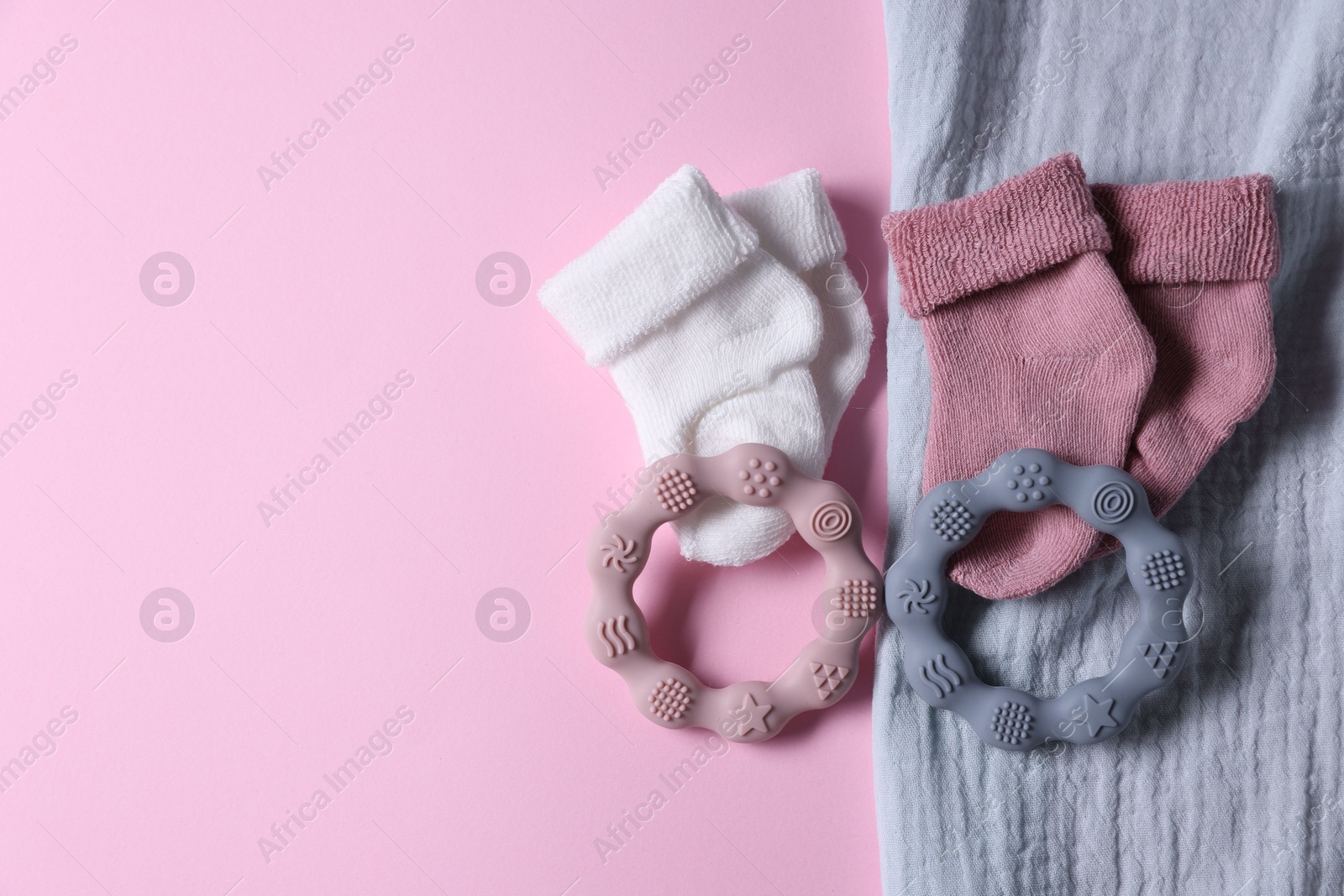 Photo of Baby blanket, socks and teethers on pink background, flat lay. Space for text