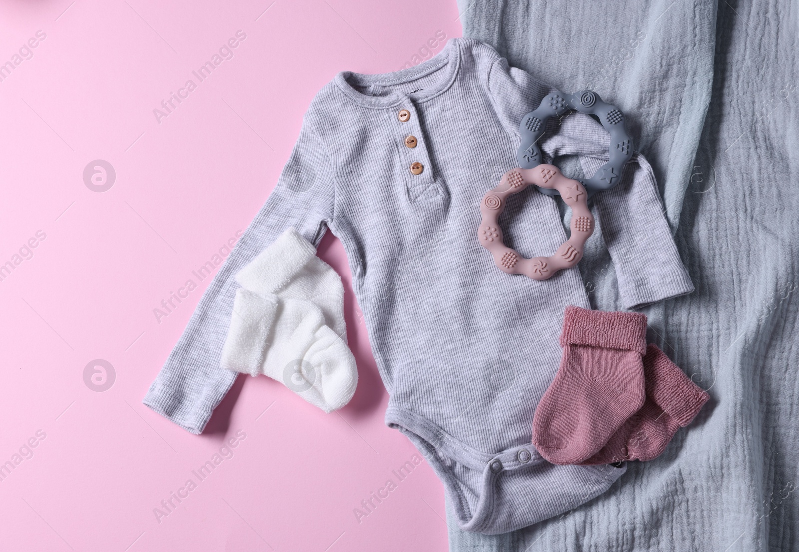 Photo of Baby clothes, blanket and teethers on pink background, flat lay