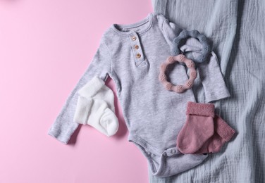 Baby clothes, blanket and teethers on pink background, flat lay