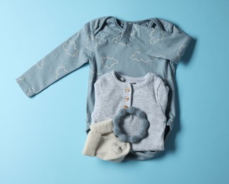 Photo of Baby clothes and teether on light blue background, flat lay