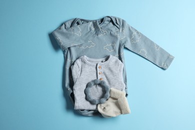 Photo of Baby clothes and teether on light blue background, flat lay