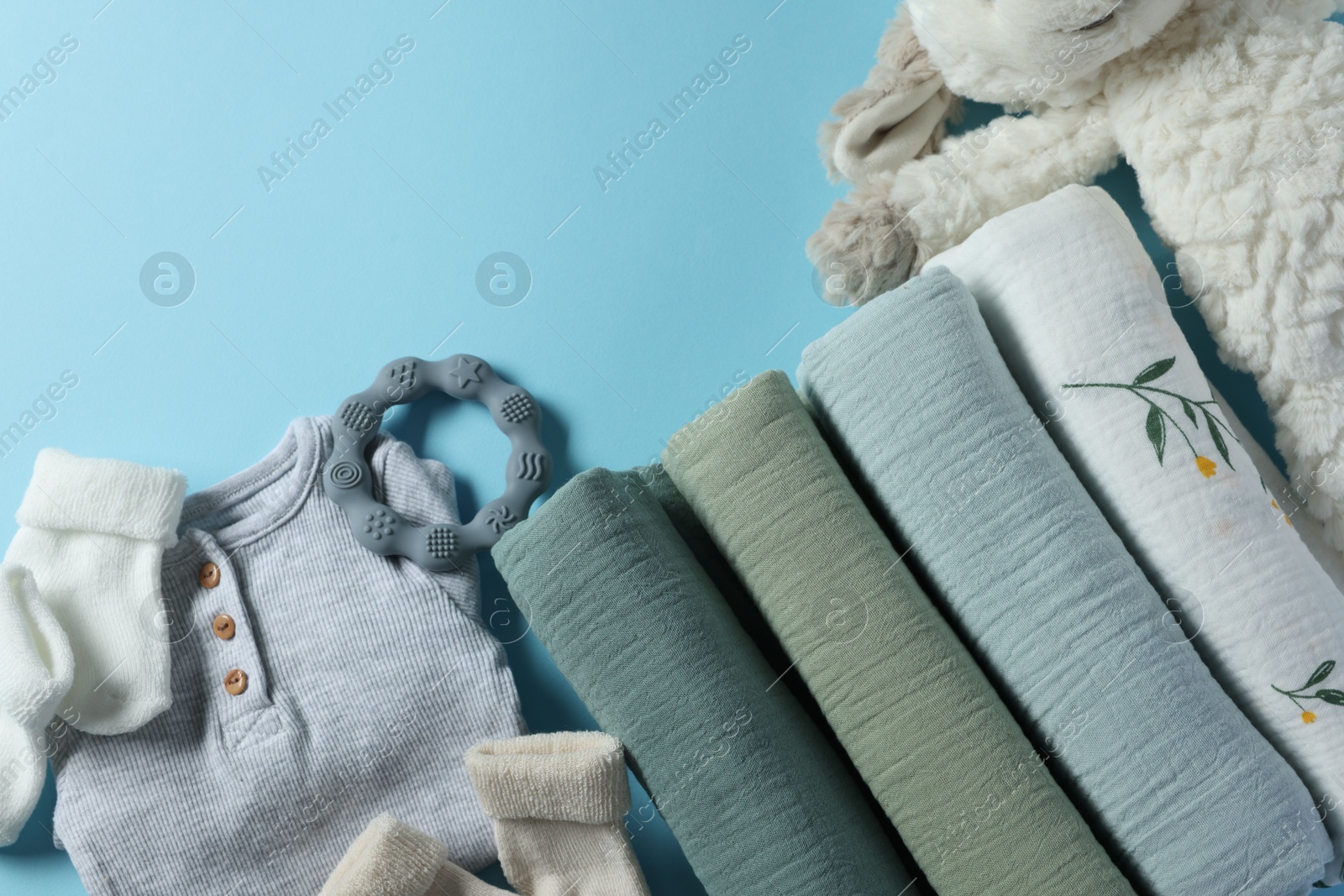 Photo of Baby clothes, rolled blankets, toy and teether on light blue background, flat lay