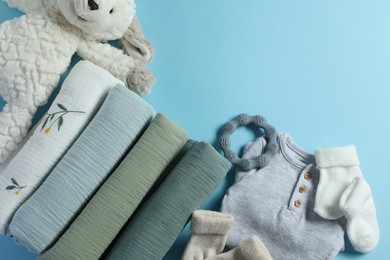 Photo of Baby clothes, rolled blankets, toy and teether on light blue background, flat lay