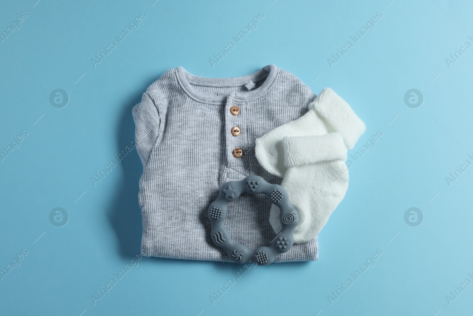 Photo of Baby clothes and teether on light blue background, flat lay