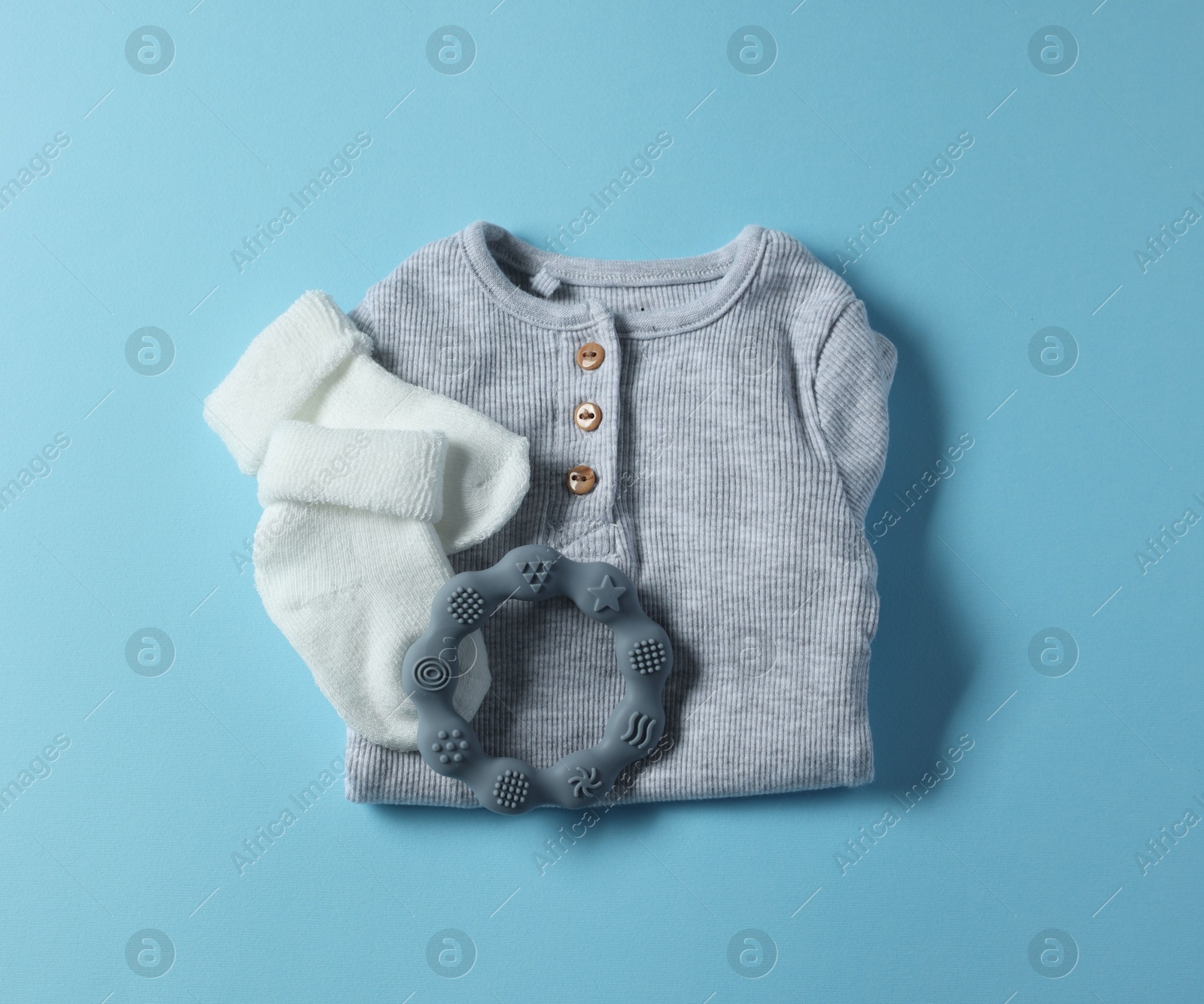 Photo of Baby clothes and teether on light blue background, flat lay