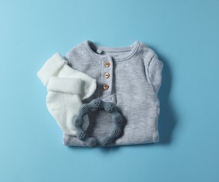 Photo of Baby clothes and teether on light blue background, flat lay