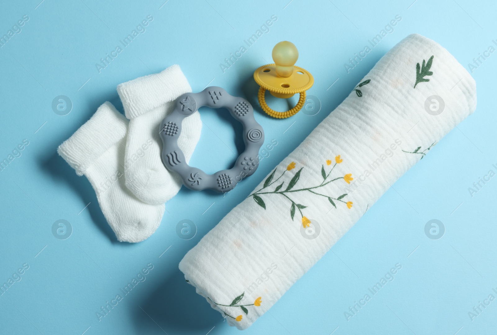 Photo of Rolled baby blanket, socks, pacifier and teether on light blue background, flat lay