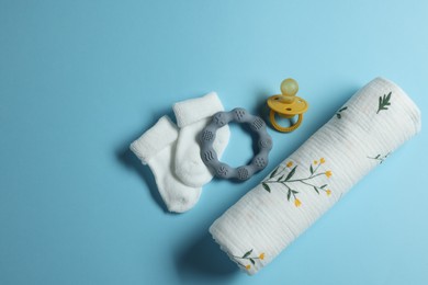 Rolled baby blanket, socks, pacifier and teether on light blue background, flat lay