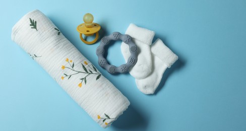 Rolled baby blanket, socks, pacifier and teether on light blue background, flat lay