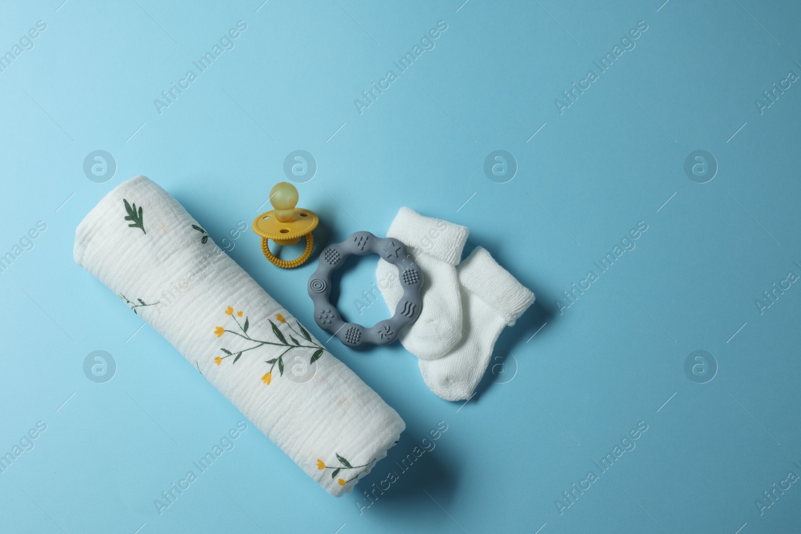 Photo of Rolled baby blanket, socks, pacifier and teether on light blue background, flat lay