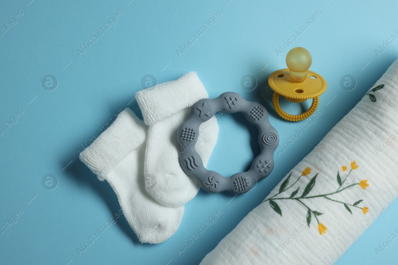 Photo of Rolled baby blanket, socks, pacifier and teether on light blue background, flat lay