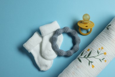 Rolled baby blanket, socks, pacifier and teether on light blue background, flat lay