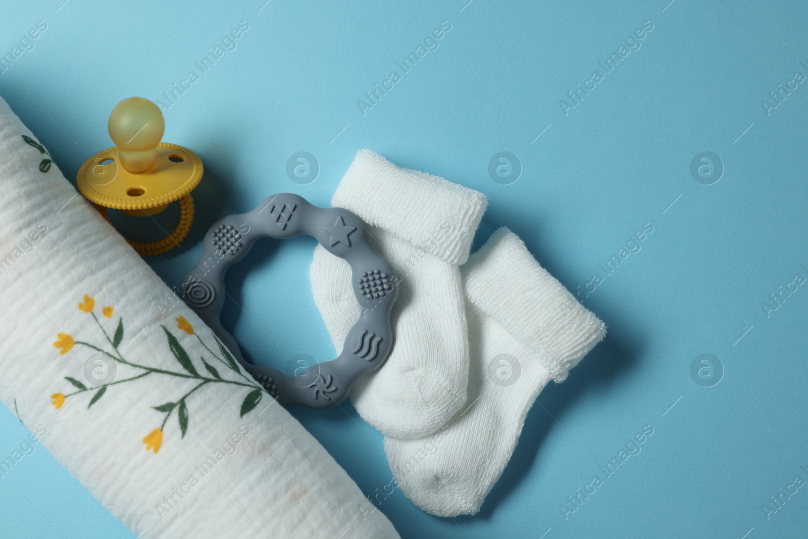 Photo of Rolled baby blanket, socks, pacifier and teether on light blue background, flat lay