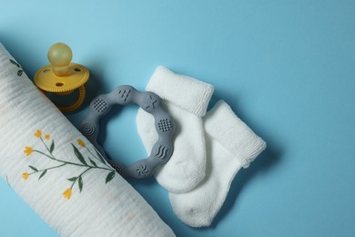 Rolled baby blanket, socks, pacifier and teether on light blue background, flat lay