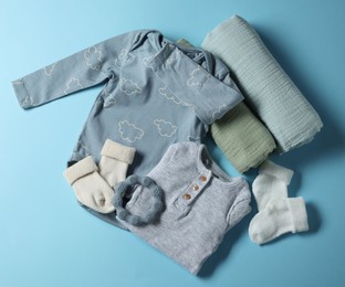 Photo of Baby clothes, rolled blankets and teether on light blue background, flat lay