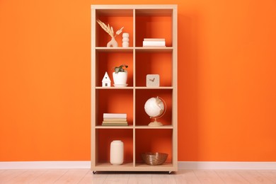 Photo of Wooden shelving unit with different home decor near orange wall indoors