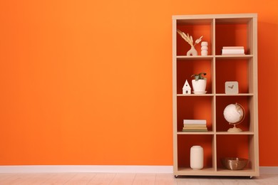 Photo of Wooden shelving unit with different home decor near orange wall indoors, space for text