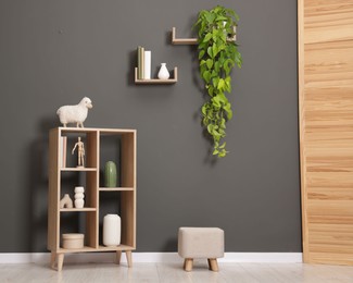 Photo of Shelving unit with different decor, folding screen and pouf near grey wall indoors