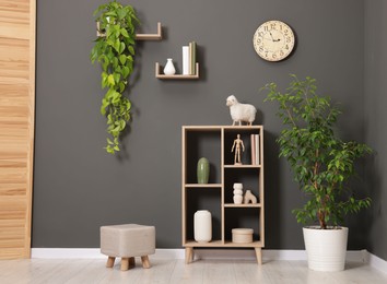 Photo of Shelving unit with different decor and pouf near grey wall indoors