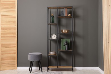 Photo of Shelving unit with decor, stool and folding screen near grey wall indoors