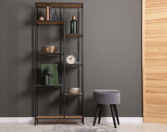 Photo of Shelving unit with decor, stool and folding screen near grey wall indoors