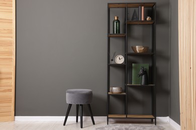 Photo of Shelving unit with decor, stool and folding screen near grey wall indoors