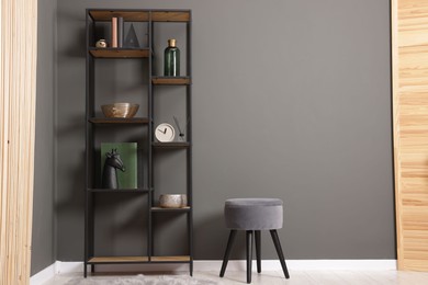 Photo of Shelving unit with decor, stool and folding screen near grey wall indoors