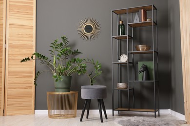 Photo of Shelving unit with decor, stool and folding screen near grey wall indoors