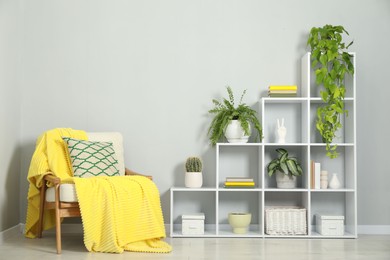 Photo of Shelving unit with green houseplants, other decor and armchair near light grey wall indoors