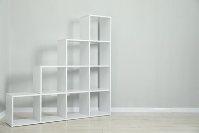 Photo of Empty shelving unit near light grey wall indoors, space for text