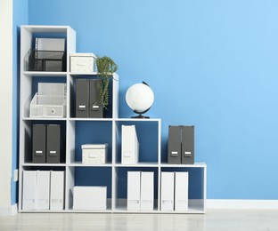 Photo of Shelving unit with folders and globe near light blue wall indoors, space for text