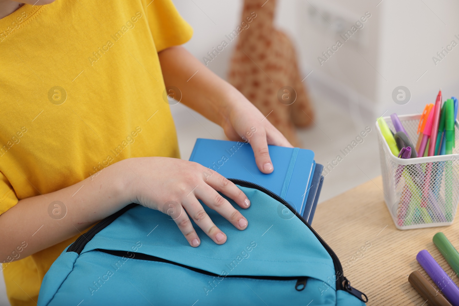 Photo of Boy packing backpack for school at wooden table indoors, closeup