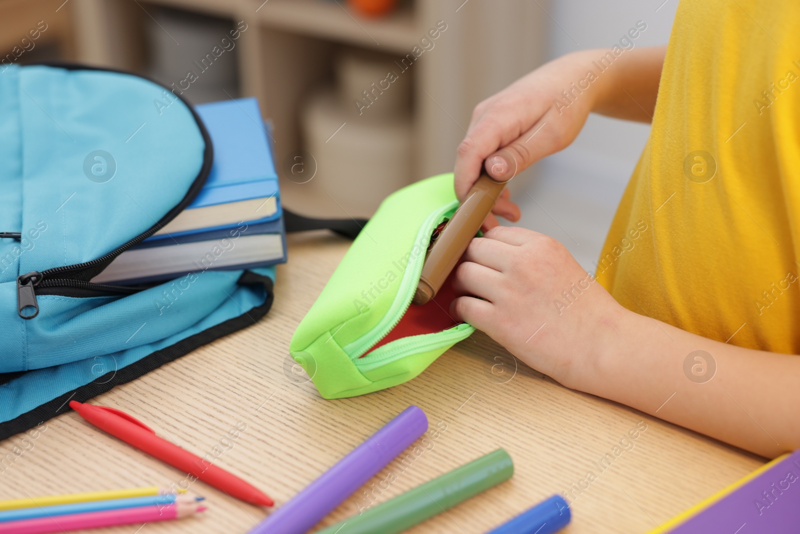 Photo of Boy packing pencil case at wooden table indoors, closeup