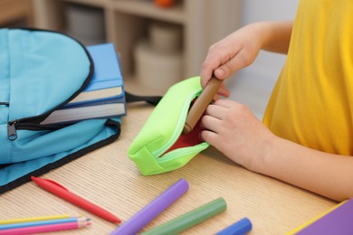 Boy packing pencil case at wooden table indoors, closeup