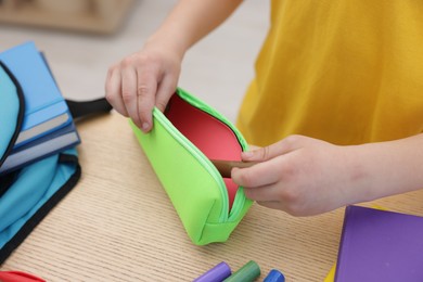 Photo of Boy packing pencil case at wooden table indoors, closeup