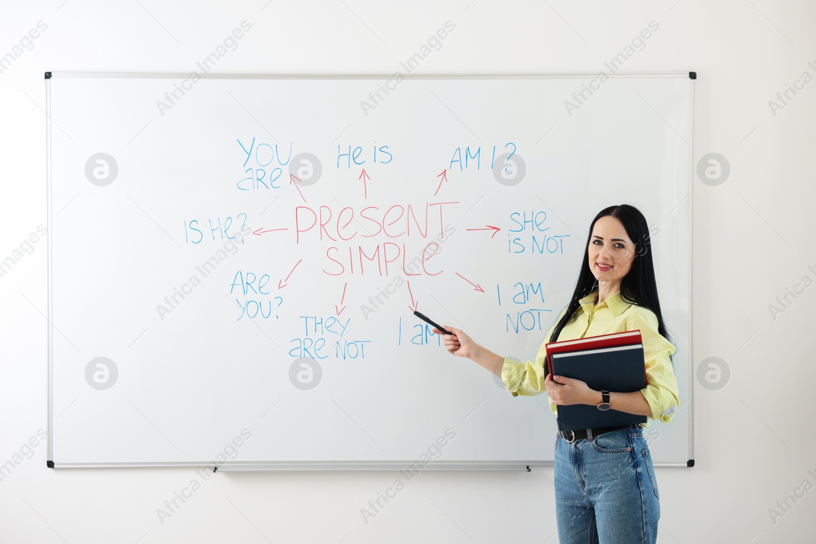 Photo of English teacher explaining Present Simple tense at whiteboard in classroom