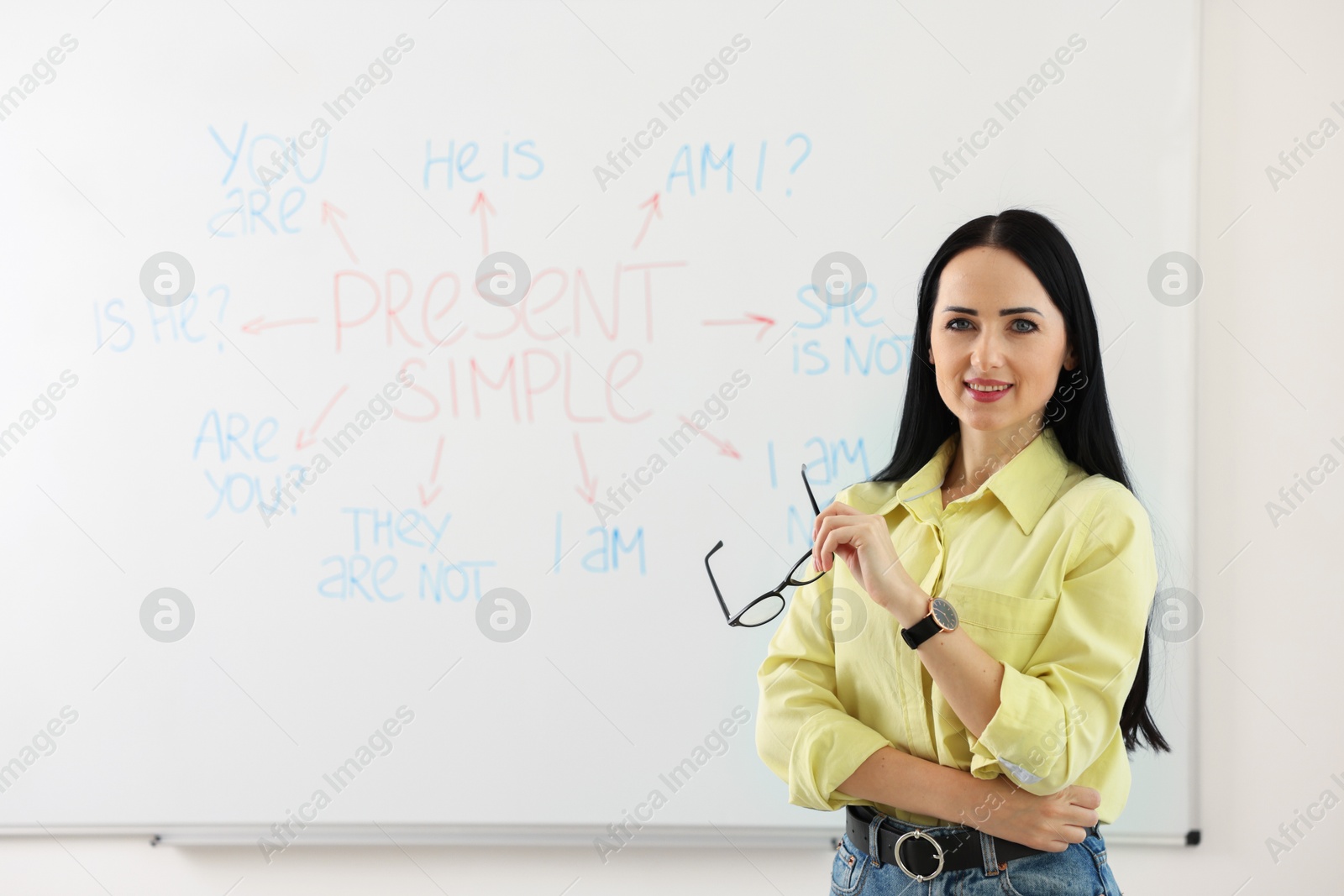 Photo of English teacher explaining Present Simple tense at whiteboard in classroom