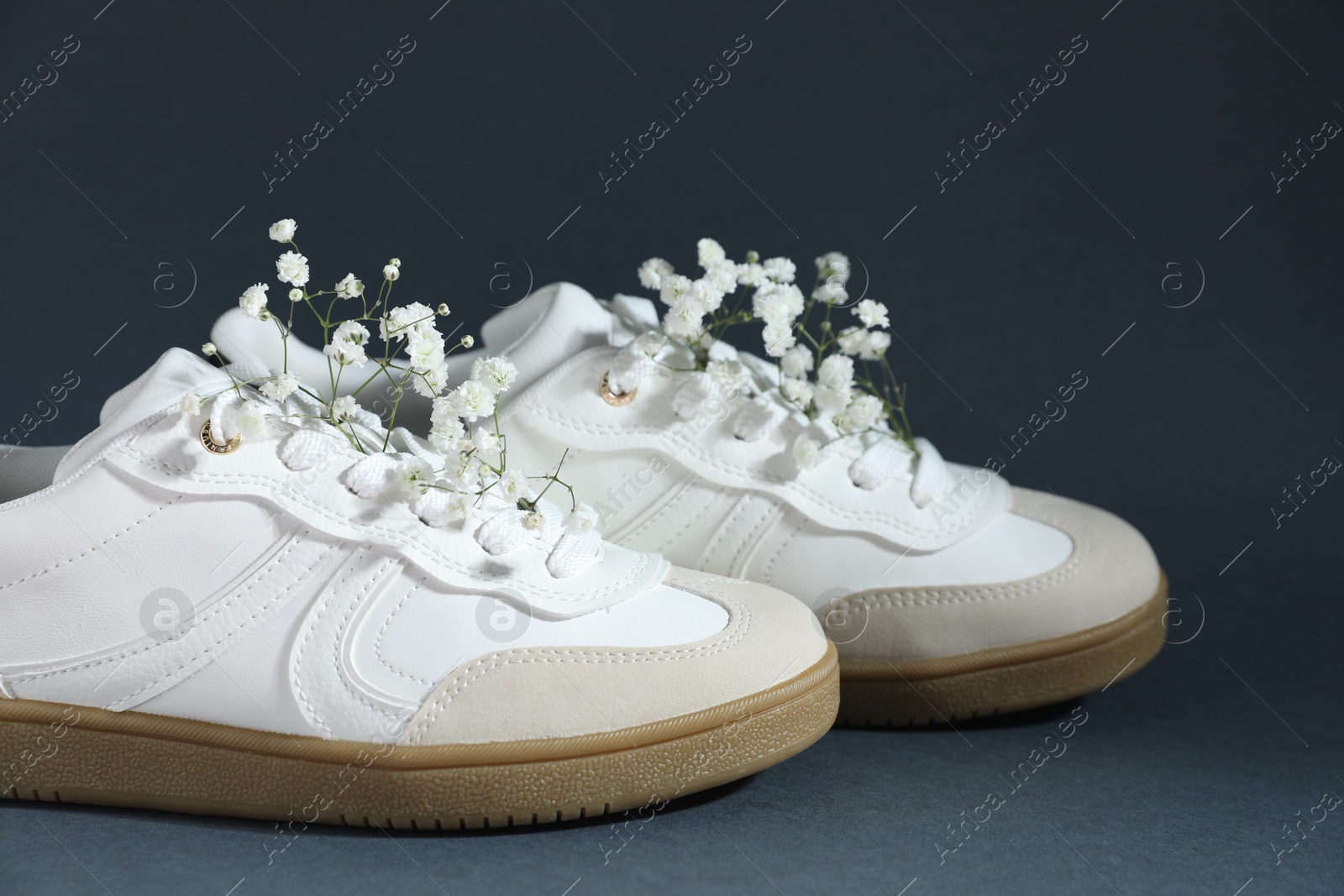 Photo of Pair of stylish sneakers and gypsophila flowers on grey background, closeup. Casual shoes