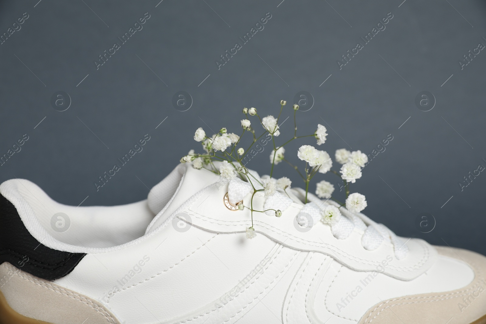 Photo of Pair of stylish sneaker and gypsophila flowers on grey background, closeup. Casual shoe