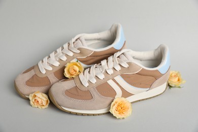 Photo of Pair of stylish sneakers and beautiful roses on light grey background. Casual shoes