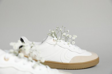 Photo of Pair of stylish sneakers and gypsophila flowers on light grey background, closeup. Casual shoes