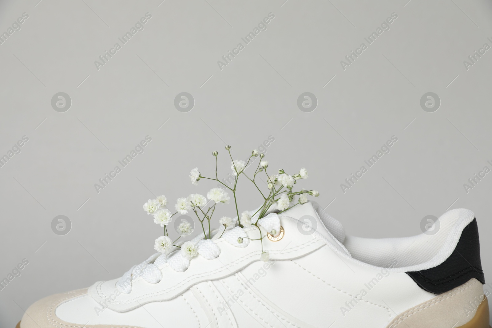 Photo of Pair of stylish sneaker and gypsophila flowers on light grey background, closeup. Casual shoe