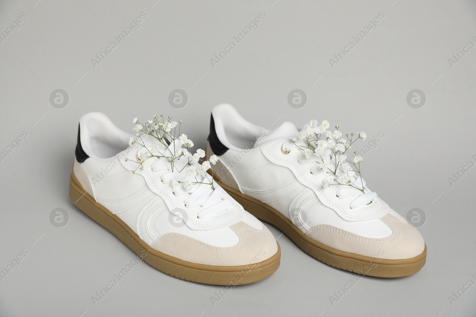 Photo of Pair of stylish sneakers and gypsophila flowers on light grey background. Casual shoes