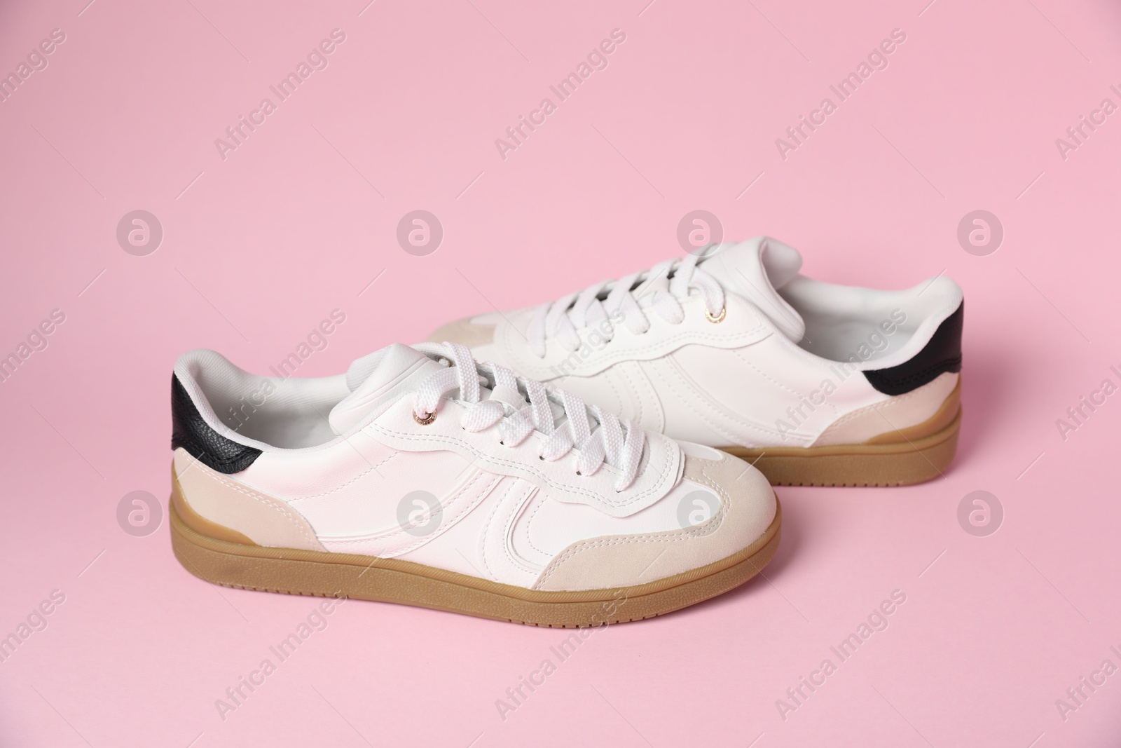 Photo of Pair of stylish sneakers on pale pink background. Casual shoes